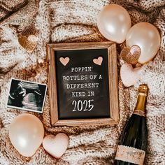 a bottle of champagne and some balloons on a blanket with a sign that says poppin bottles of a different kind in 2055