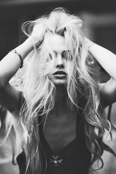 a black and white photo of a woman with her hair blowing in the wind, holding her hands to her head