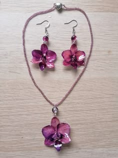 a necklace and earring set with purple flowers on a wooden surface, one is attached to a chain