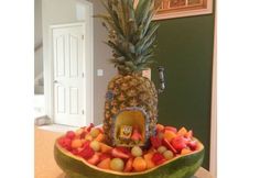 a large bowl filled with lots of fruit on top of a wooden table next to a doorway