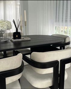 a dining room table and chairs with white flowers in vases on the top shelf