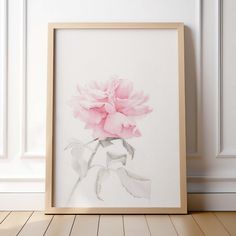 a watercolor painting of a pink flower in a wooden frame against a white wall