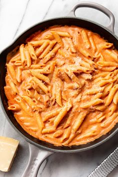 a skillet filled with pasta and sauce on top of a white counter next to cheese