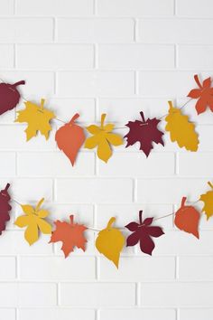 fall leaves are hanging on a string against a white brick wall