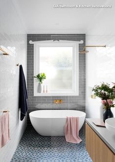 a white bath tub sitting under a window next to a sink in a bathroom with blue tile