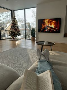 a person sitting on a couch reading a book in front of a christmas tree and fireplace