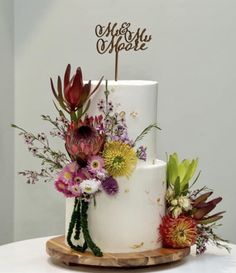 a three tiered cake with flowers and a wooden sign on top that says she & him aparte