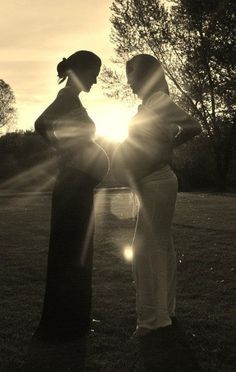 two women standing next to each other on top of a grass covered field with the sun behind them