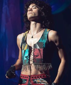 a man with long hair and no shirt on standing in front of a blue background