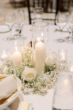 a centerpiece with white flowers and candles on a round table in front of wine glasses