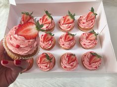 a person is holding up a box of cupcakes with strawberries on top