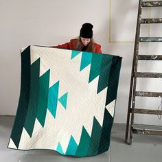 a woman is holding a large quilt in front of her face and leaning on a ladder