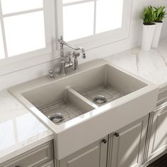 a white kitchen sink with two faucets in the middle and a window behind it