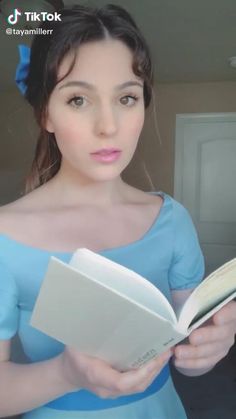 a woman in a blue dress is holding a book and looking at the camera with an intense look on her face