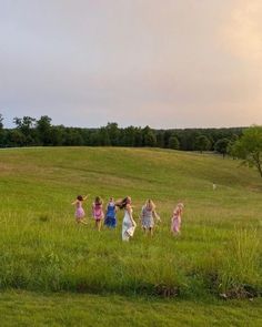 four girls are walking in the grass with their arms around each other and one girl is flying a kite