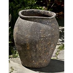 a large stone vase sitting on top of a cement floor next to plants and trees