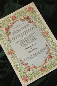 an ornate wedding card with pink flowers and green trimmings on a black background