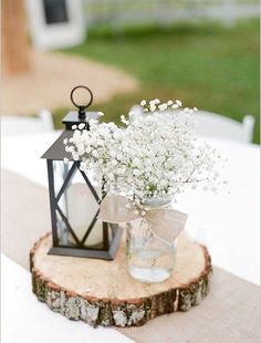 a vase filled with white flowers sitting on top of a wooden table next to a lantern