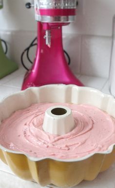 a cake pan filled with pink icing next to a stand mixer on a counter