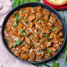 meat and vegetable stew in a skillet on a table next to a bowl of mashed potatoes