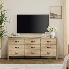 a flat screen tv mounted on top of a wooden dresser in a living room next to a window