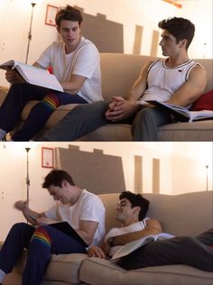 two men are sitting on a couch and one is reading a book while the other looks at something