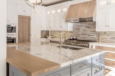 a kitchen with white cabinets and marble counter tops, an island in the middle is surrounded by stainless steel appliances