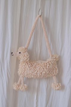 a stuffed poodle hanging on a white wall in the shape of a purse with tassels