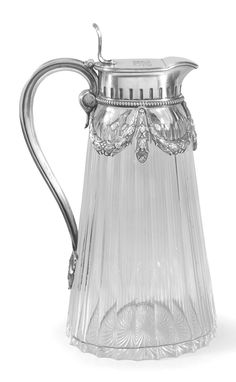 a clear glass pitcher with a silver handle and an ornate design on the top,