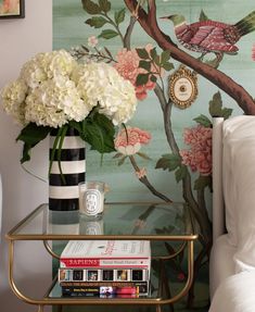 a glass table topped with flowers next to a wallpaper covered in birds and branches