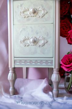 a white dresser with pink roses in the background