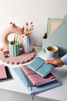 a person holding a notebook on top of a desk next to a cup of coffee