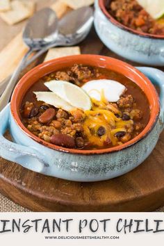 two bowls filled with chili and cheese on top of a wooden cutting board next to crackers