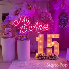 a table topped with lots of pink and white balloons next to a large neon sign