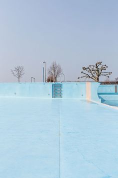 an empty swimming pool with blue walls and trees in the backgroung area