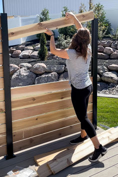 a woman holding up a piece of wood on top of a wooden deck next to some rocks