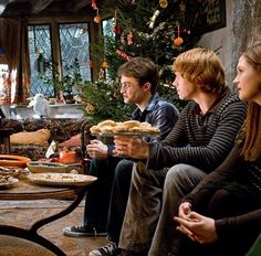 three people sitting in front of a christmas tree with food on the table and one person holding a plate