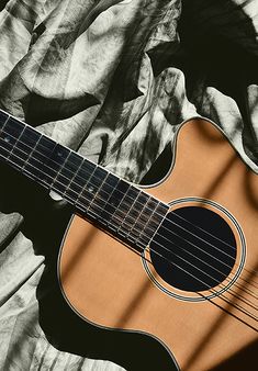 an acoustic guitar laying on top of a bed next to a blue and white blanket