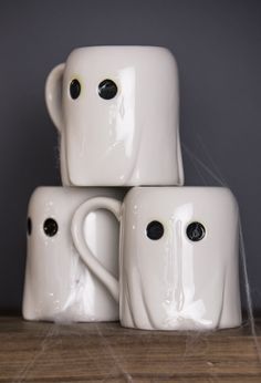 three white ceramic coffee mugs stacked on top of each other with eyes and noses