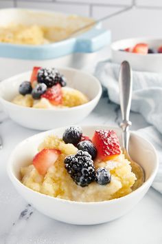 two white bowls filled with food on top of a counter next to a bowl of fruit