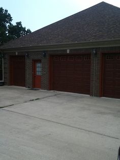 two brown garage doors are open in front of a brick building with an asphalt driveway