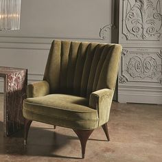 a green chair sitting next to a small table in a room with a chandelier hanging from the ceiling