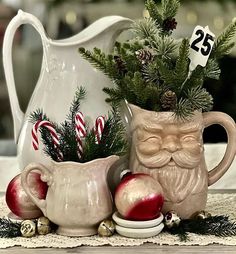 a white pitcher filled with christmas decorations on top of a table next to other items