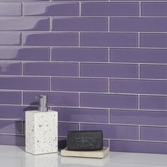 a soap dispenser sitting on top of a counter next to a purple tiled wall