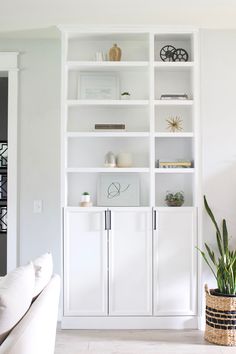 a living room filled with white furniture and bookshelves next to a plant in a pot