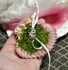 someone is holding a tiny ornament with moss and pearls on it, in their hand