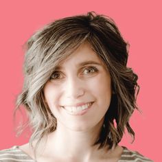 a woman with grey hair smiling and wearing a striped shirt against a pink background,