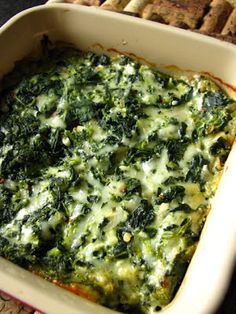 a casserole dish with spinach, cheese and bread in it on a table