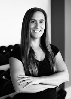 a woman standing with her arms crossed in front of a rack of dumbbells