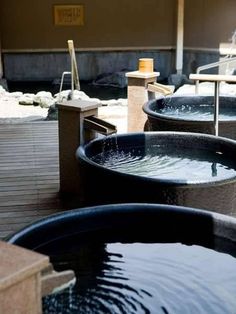 several large black bowls filled with water sitting on top of a wooden floor next to benches